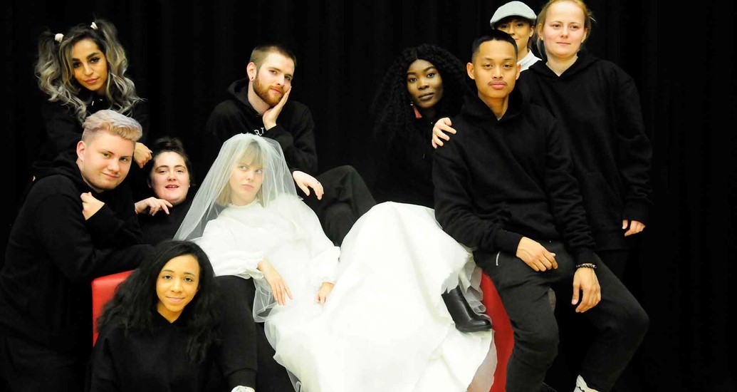 Image of group of people dressed in black, with woman in wedding dress in the middle