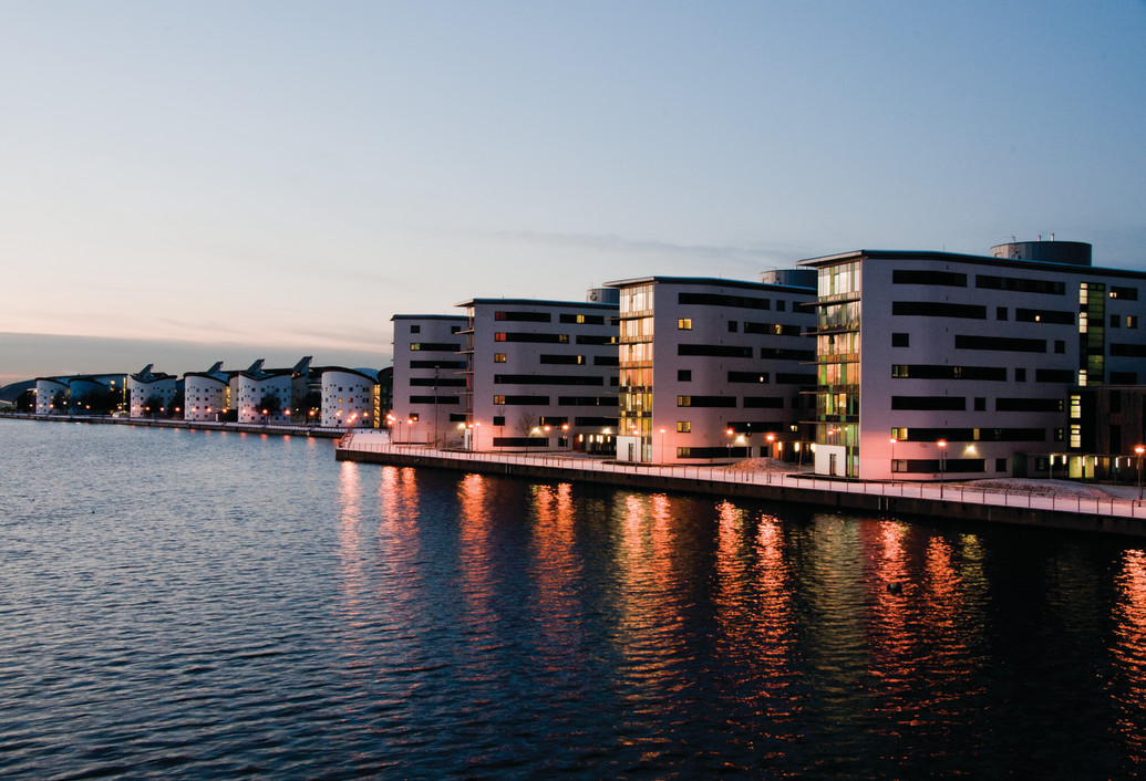 Docklands Campus at dusk with lights from the buildings reflecting on the water surface