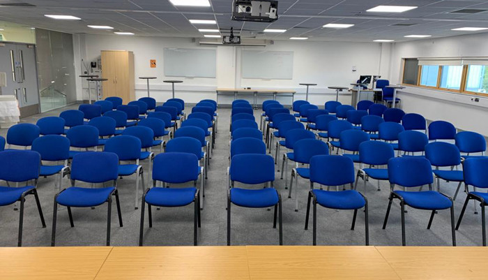 Glass room at UEL with rows of blue chairs.