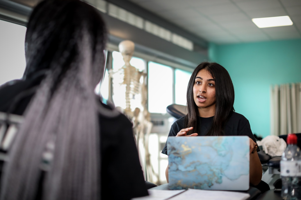 Two students in a sports lab chatting in front of a skeleton