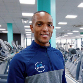 Personal Trainer wearing a blue sports jacket in the gym at SportsDock in front of a row of treadmills.