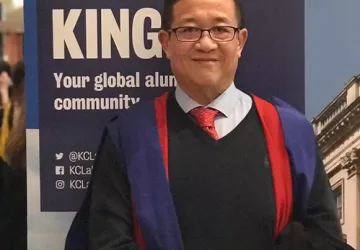 Dr Steve Wong stands smiling wearing a graduation gown 