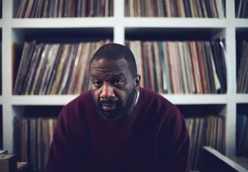Tony Nwachukwu looking into the camera in front of shelves of records.