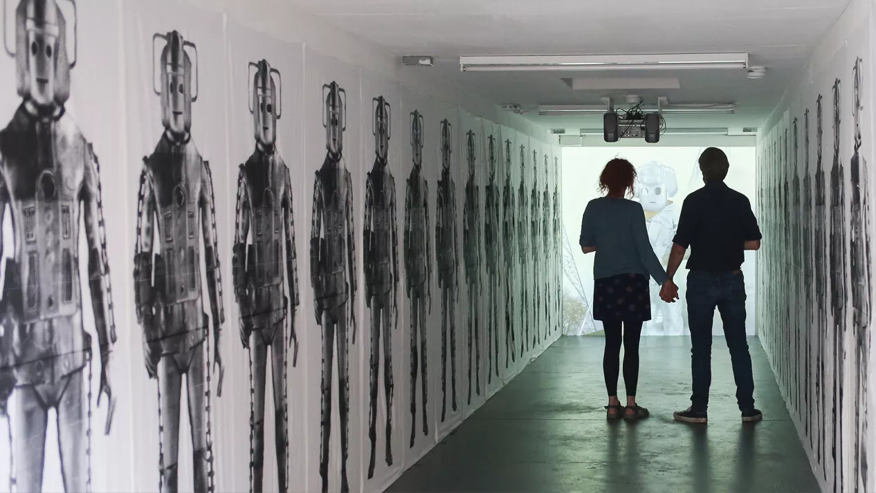 Two people standing in a hallway with Doctor Who Cybermen painting on the walls