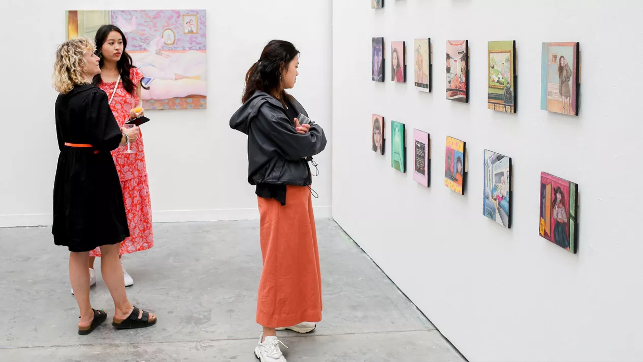 Three women looking at painting hung on a wall