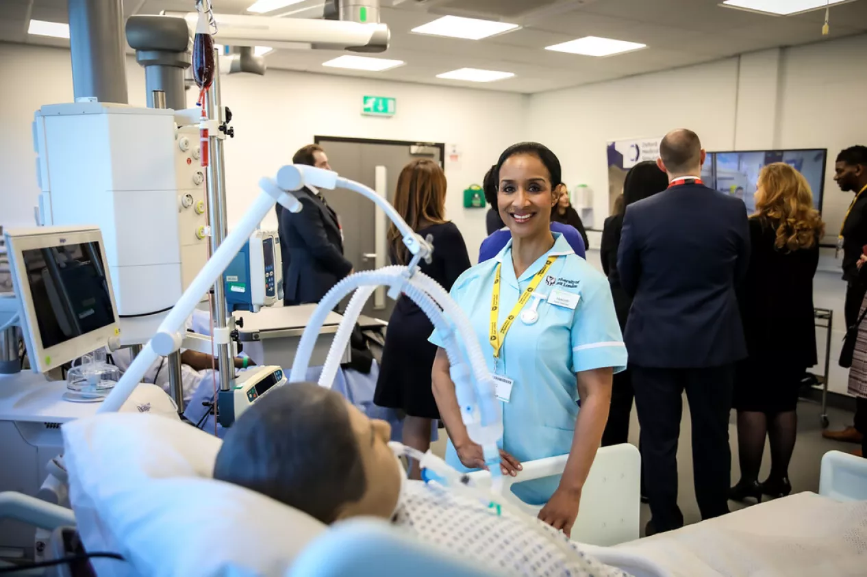 A nursing student smiling at the camera next to a training hospital bed