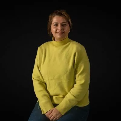  a woman in a yellow sweater sitting on a stool. 